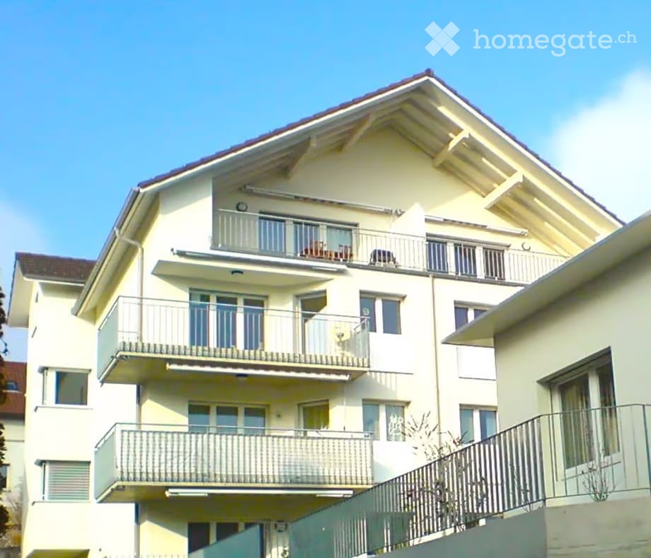 3 story apartment building, white walls, red roof, multiple balconies, window shutters
