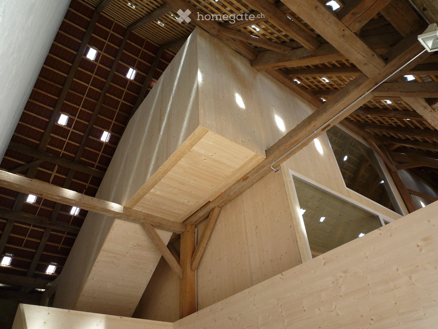 Wooden staircase with exposed beams and skylights, leading to an upper level.
