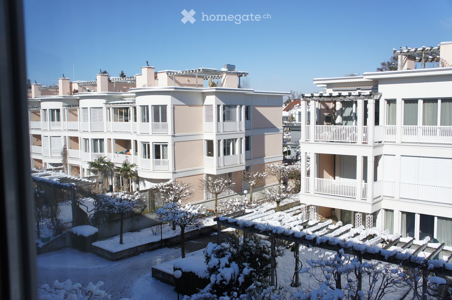 A multi-story residential building complex with balconies and snow-covered ground and trees.