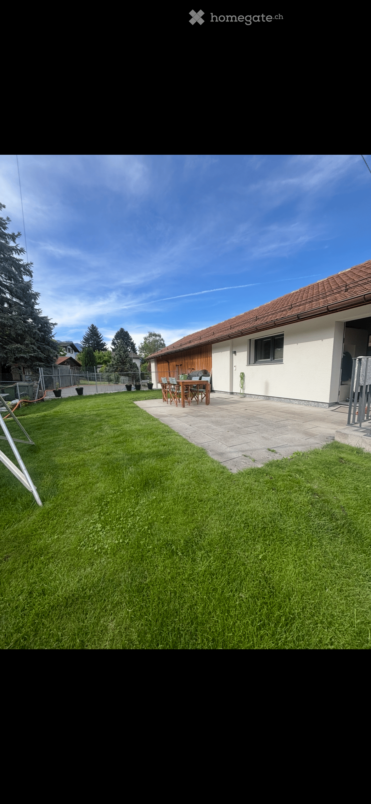 Well-maintained garden with a neatly trimmed lawn, a paved patio area, and a wooden table with chairs near the house.