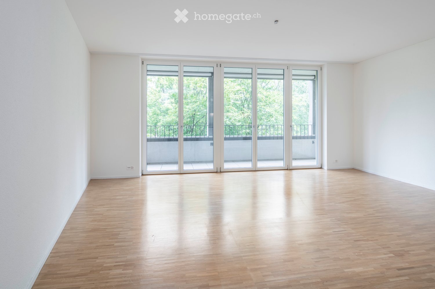 Empty room with wooden flooring, white walls, and large sliding glass doors leading to a balcony.