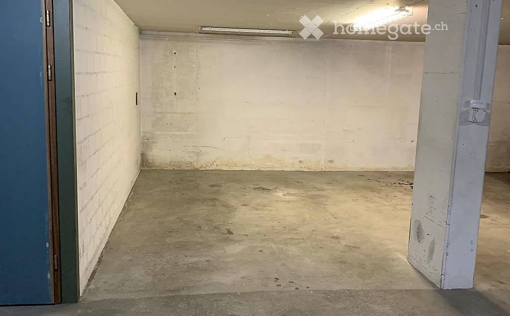 Empty garage with brick walls and concrete floor, ceiling lights, a column in the right corner.