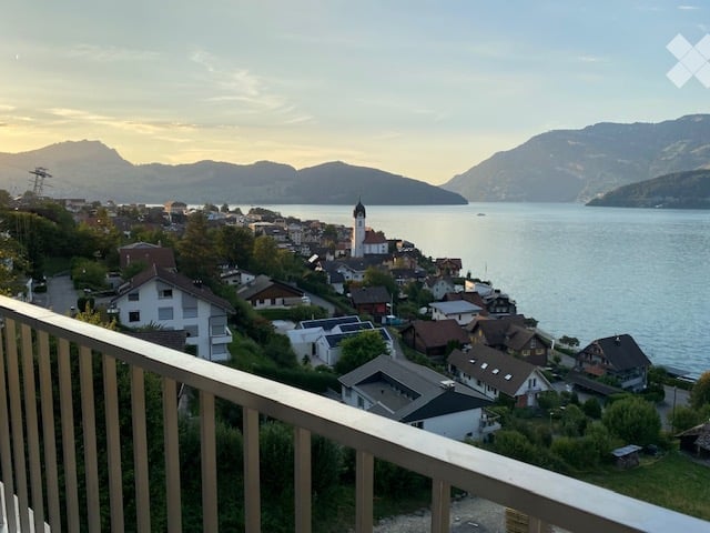 Balcony overlooking a picturesque lakeside town with houses, a church, and mountains in the background.