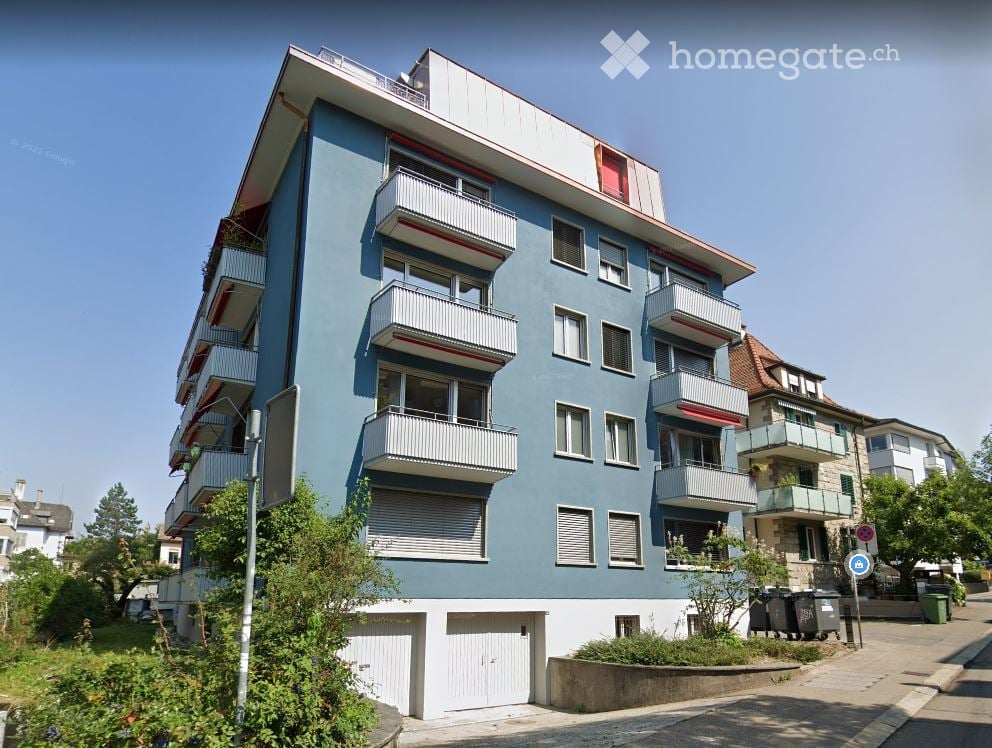 Modern multi-story apartment building with blue facade, white balconies, and garage entrances.