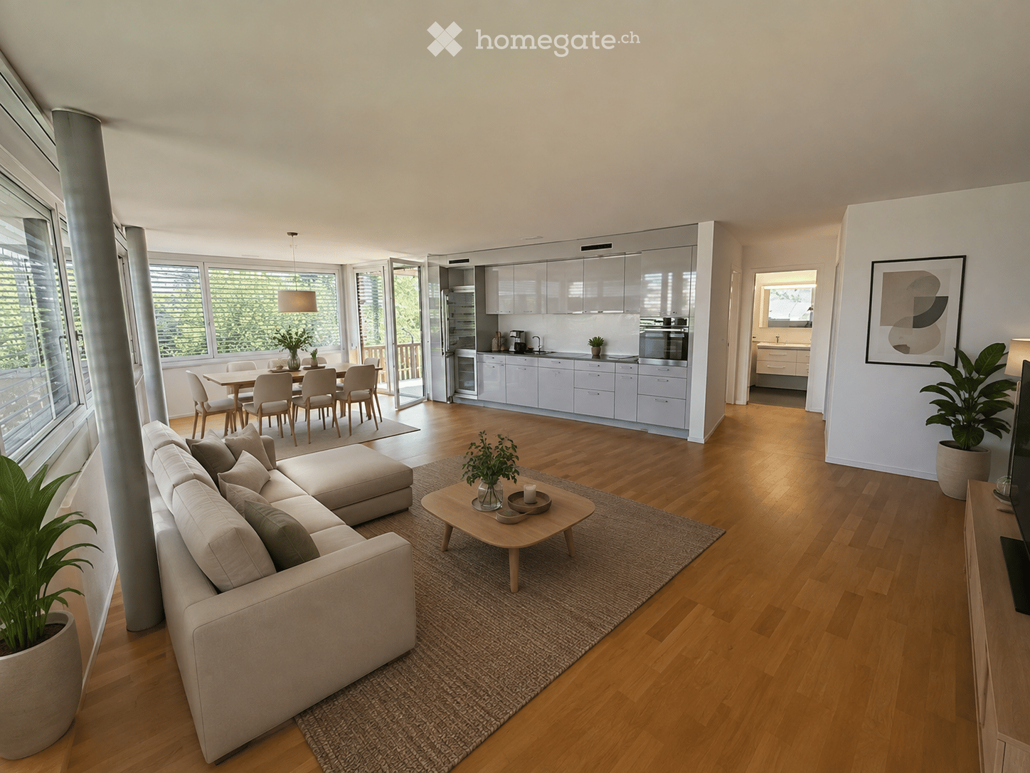 Modern open-plan living and dining area with light wood flooring, large windows, a sectional sofa, coffee table, dining table with chairs, and a sleek kitchen with white cabinets and stainless steel appliances.