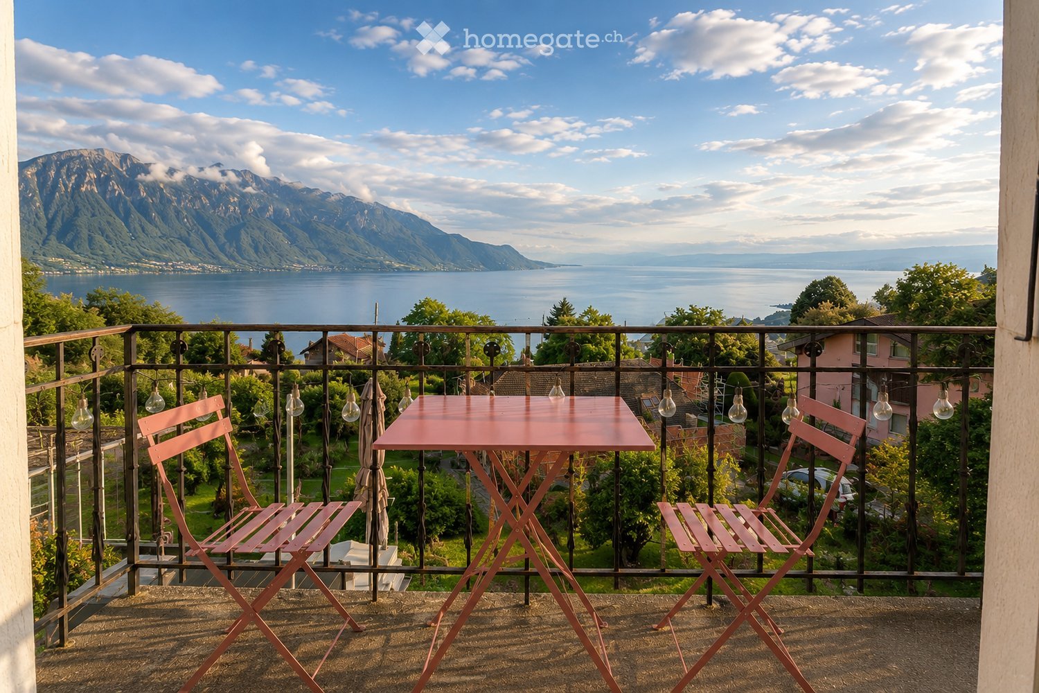 Balcony with a table and two chairs, overlooking a scenic lake and mountain view.