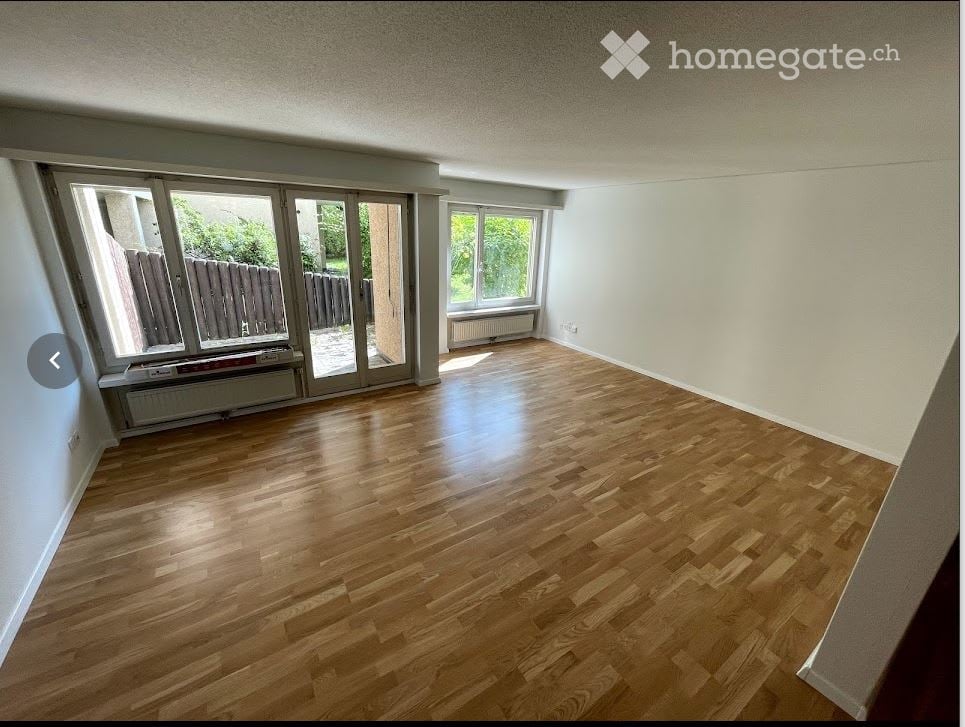 Empty room with wooden flooring, large windows, and sliding glass doors leading to an outdoor area.
