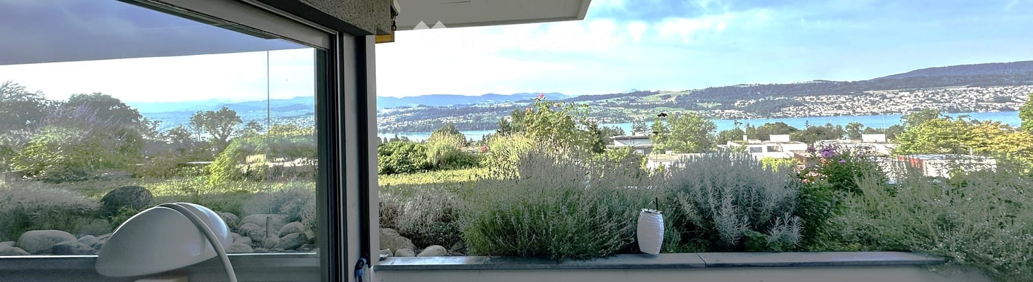 Balcony with a scenic view of a coastal city, mountains, and water, featuring plants and a decorative lantern.