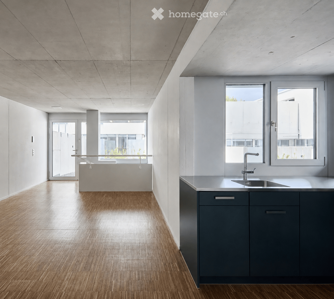 Modern, minimalist unfurnished room with polished wooden flooring, white walls, and large windows allowing natural light. The space features a sleek, contemporary design with a simple, uncluttered aesthetic.