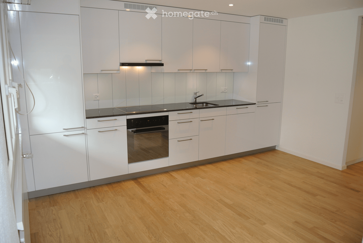 Modern kitchen with white cabinets, wooden flooring, stainless steel appliances, and a black countertop.