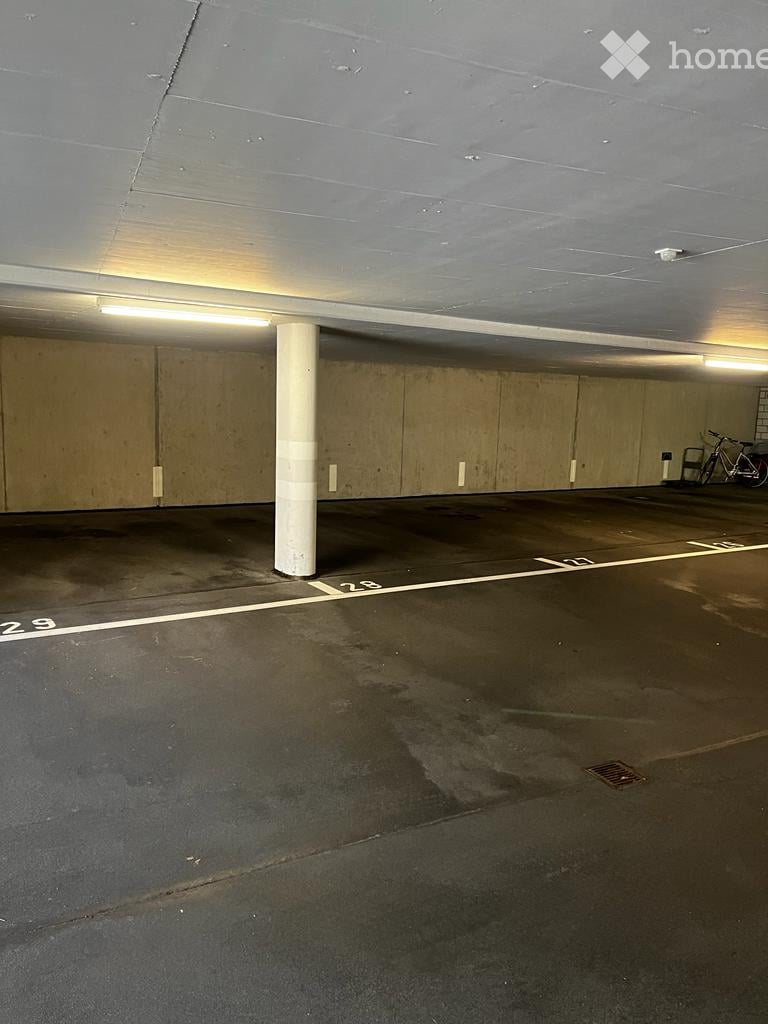 Underground parking area with marked parking spaces, a central support column, and a bicycle parked against the wall.