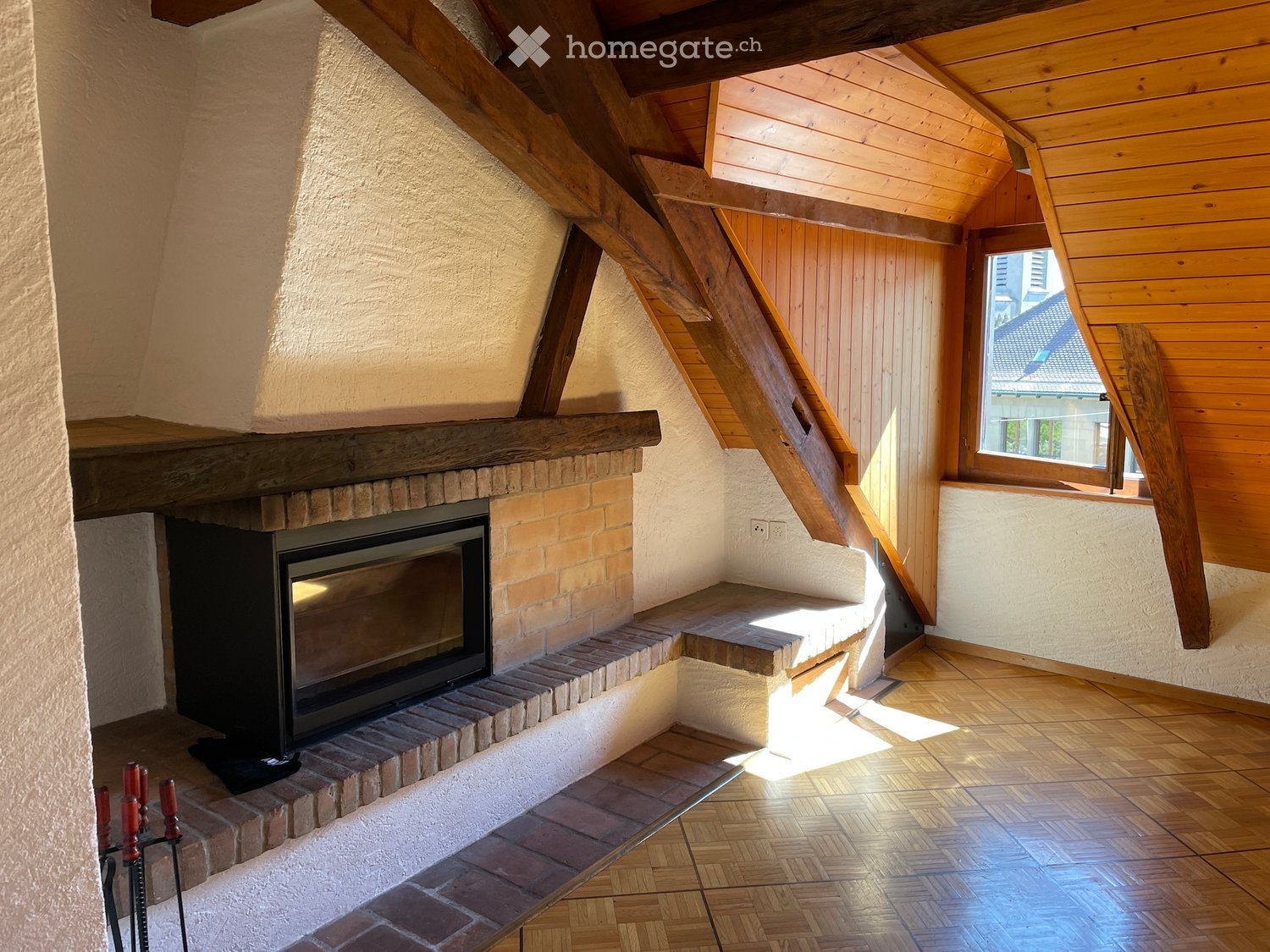 Living room with exposed wooden beams, a brick fireplace, wooden flooring, and a window letting in natural light.