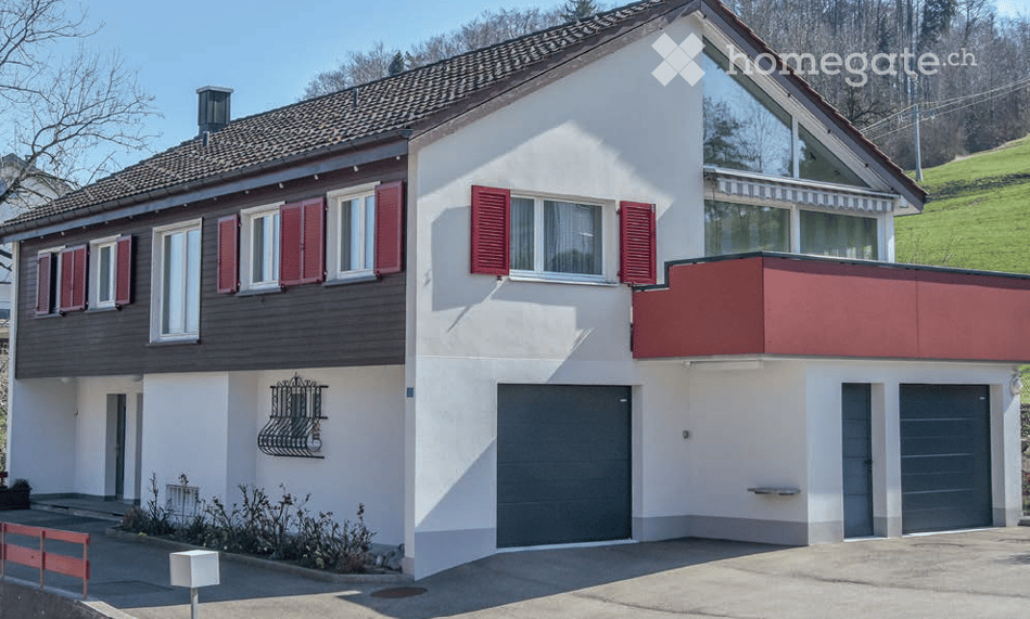 Two-story house with red shutters, white walls, grey garage doors, and a balcony on the upper level.