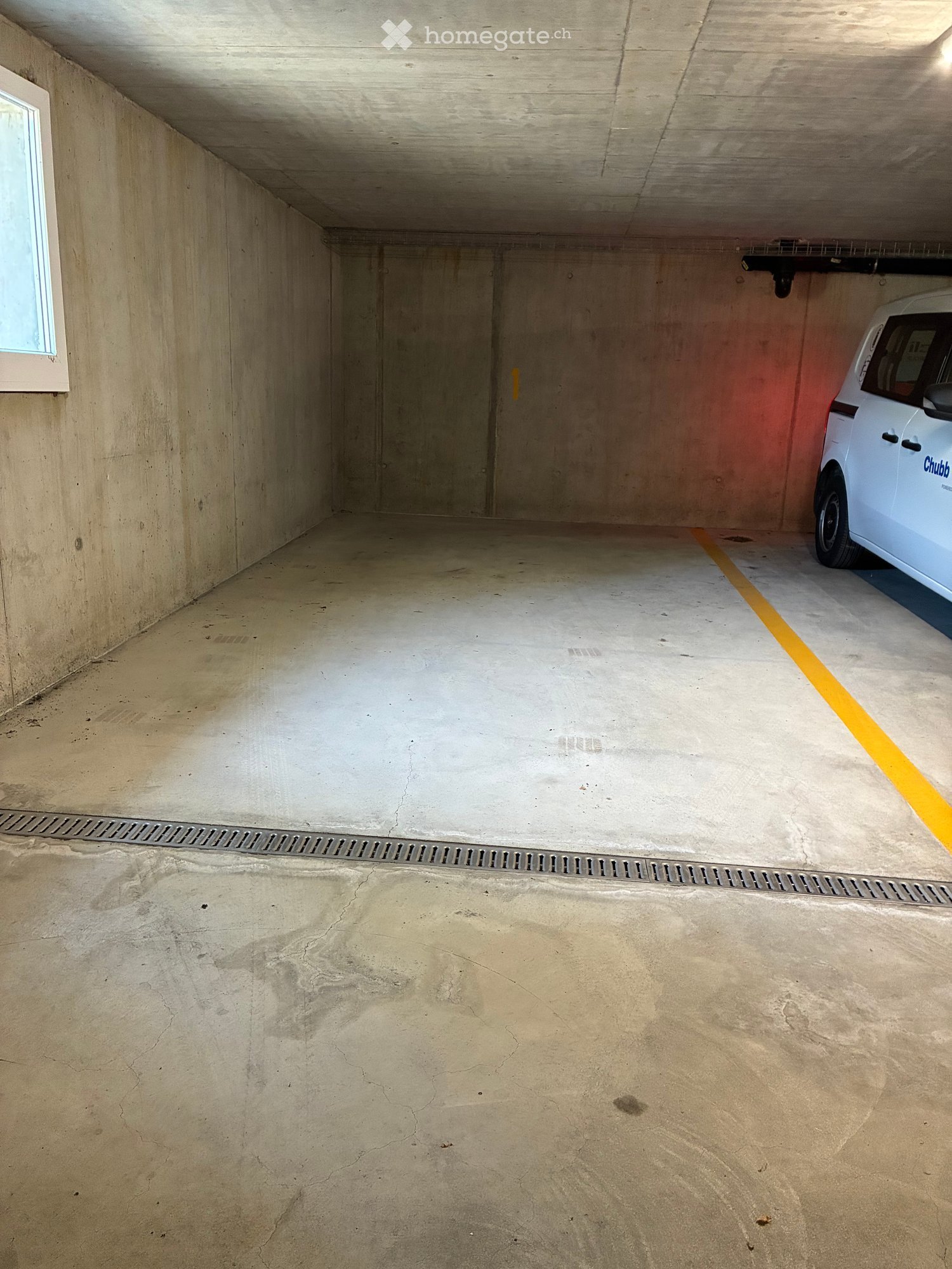 Empty underground garage with concrete walls and floor, a single parked car, and a yellow parking line.
