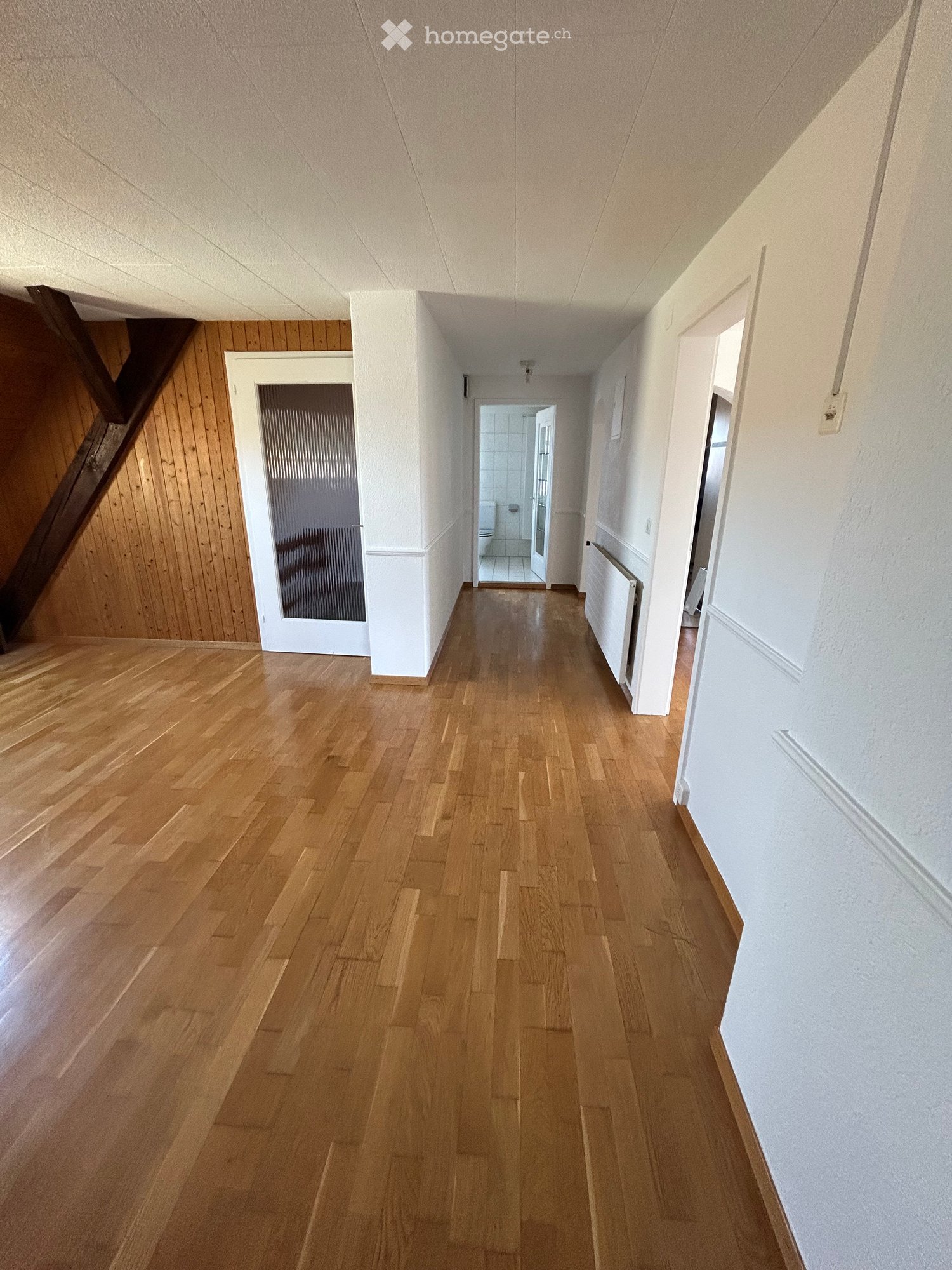 Empty hallway with wooden flooring, white walls, and several doors leading to different rooms.