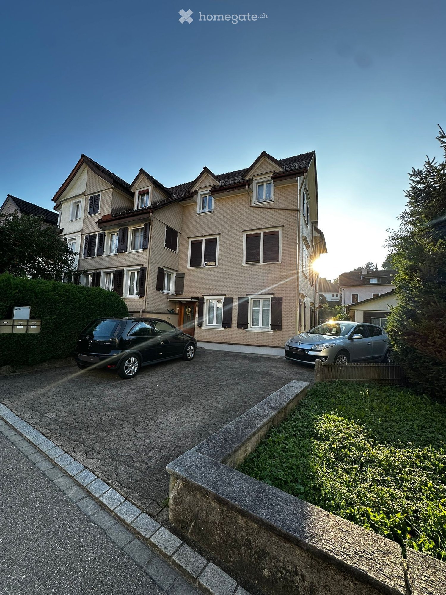 A large multistory house, with a driveway in front and two cars parked in it.