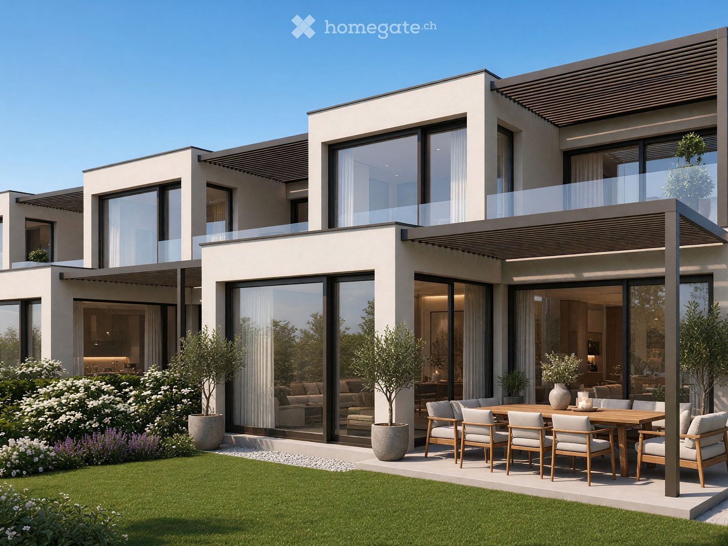 Modern two-story house with large windows and a spacious outdoor patio area featuring a wooden dining table, chairs, and potted plants.