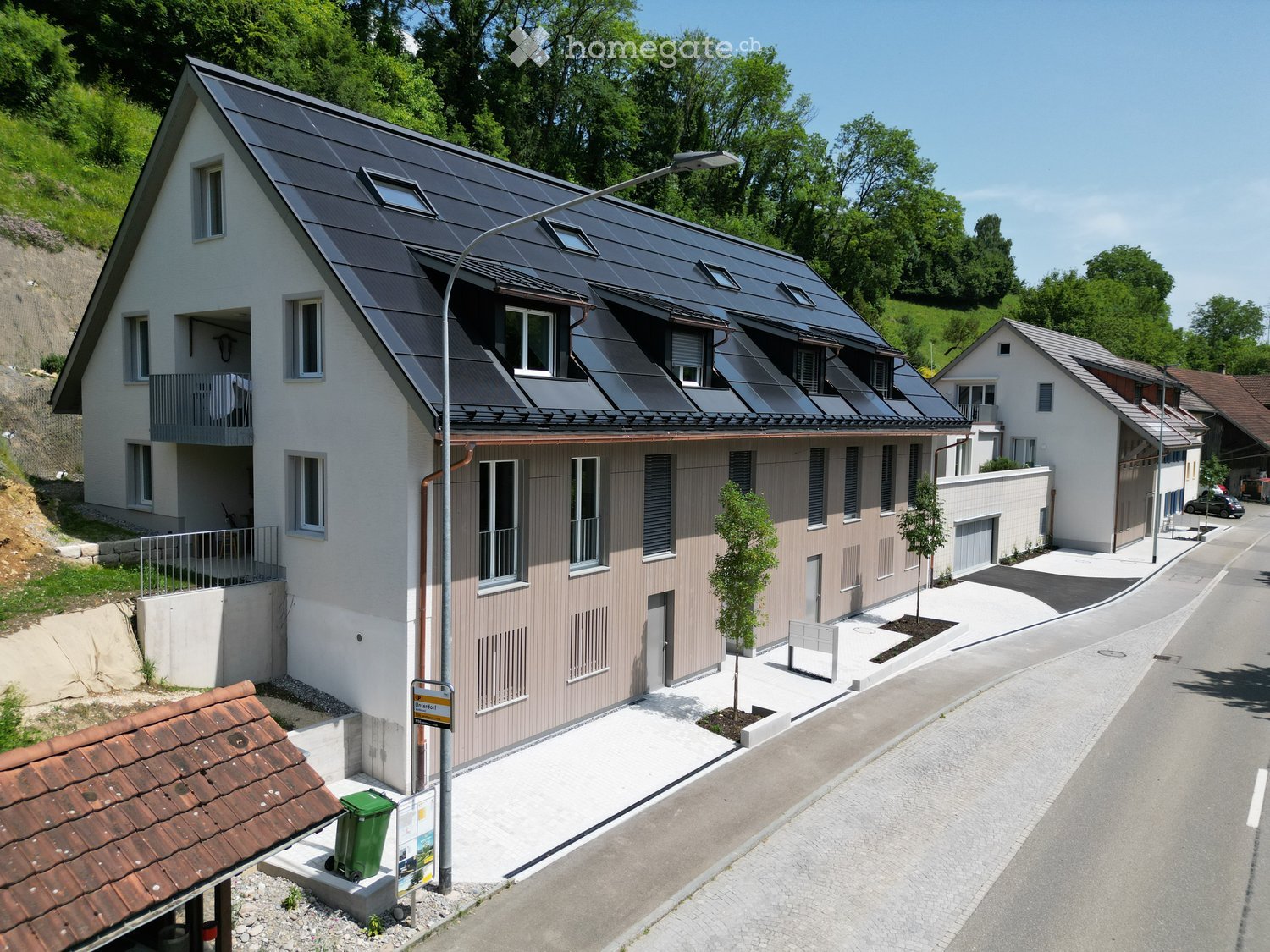 Modern two-story house with solar panels on the roof, white and brown exterior, multiple windows, and a small balcony on the upper level.