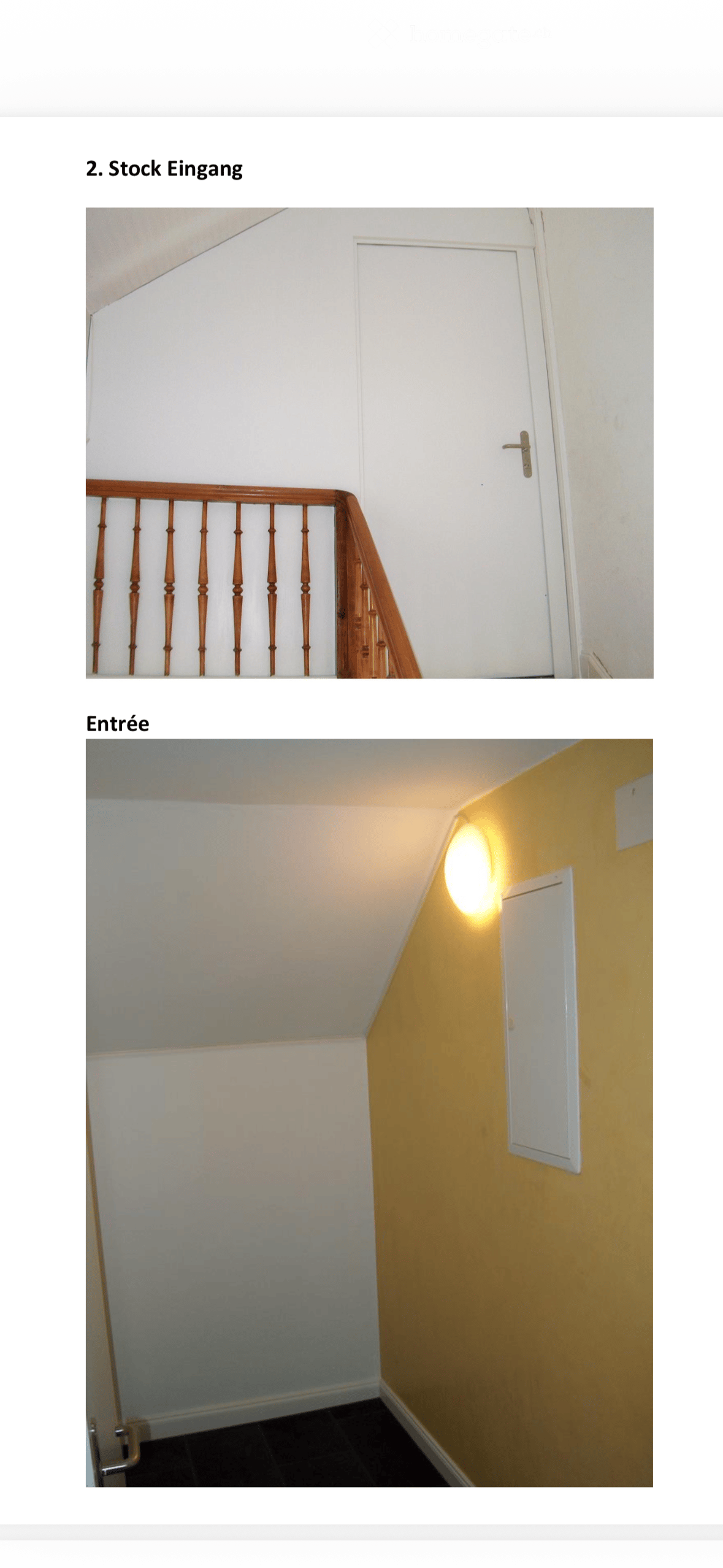 The image shows a narrow hallway with a wooden staircase railing on the left and a white door on the right. The walls are painted in neutral tones, and the floor appears to be tiled.