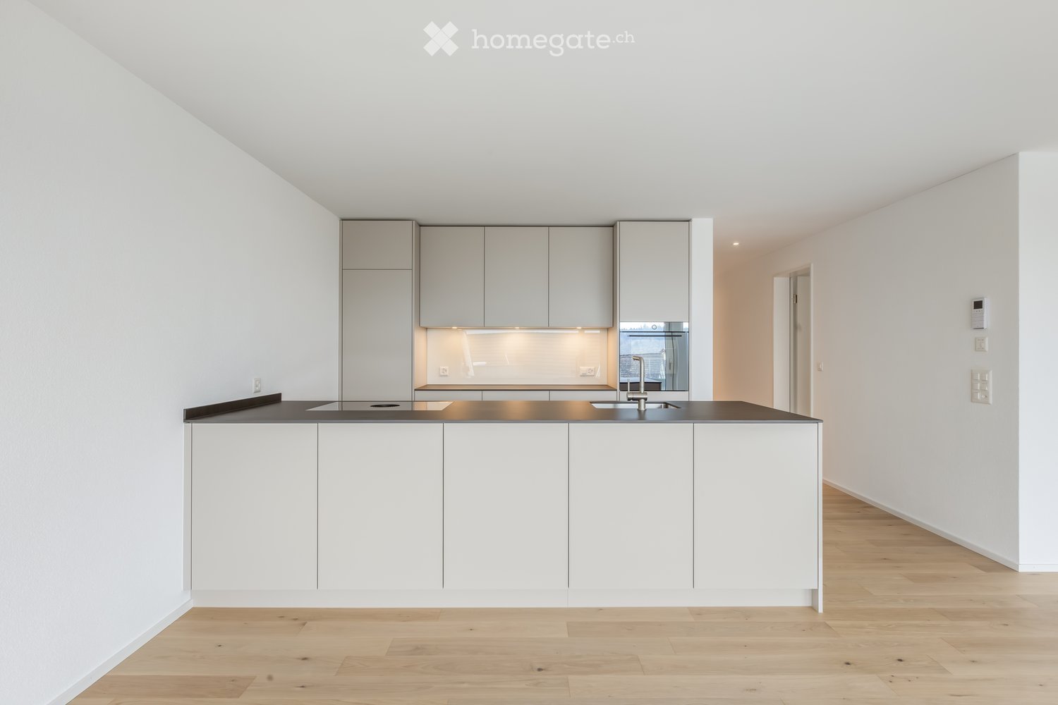 Modern kitchen with white cabinets, a central island, and a dark countertop. Features include a sink with a modern faucet and an integrated oven.