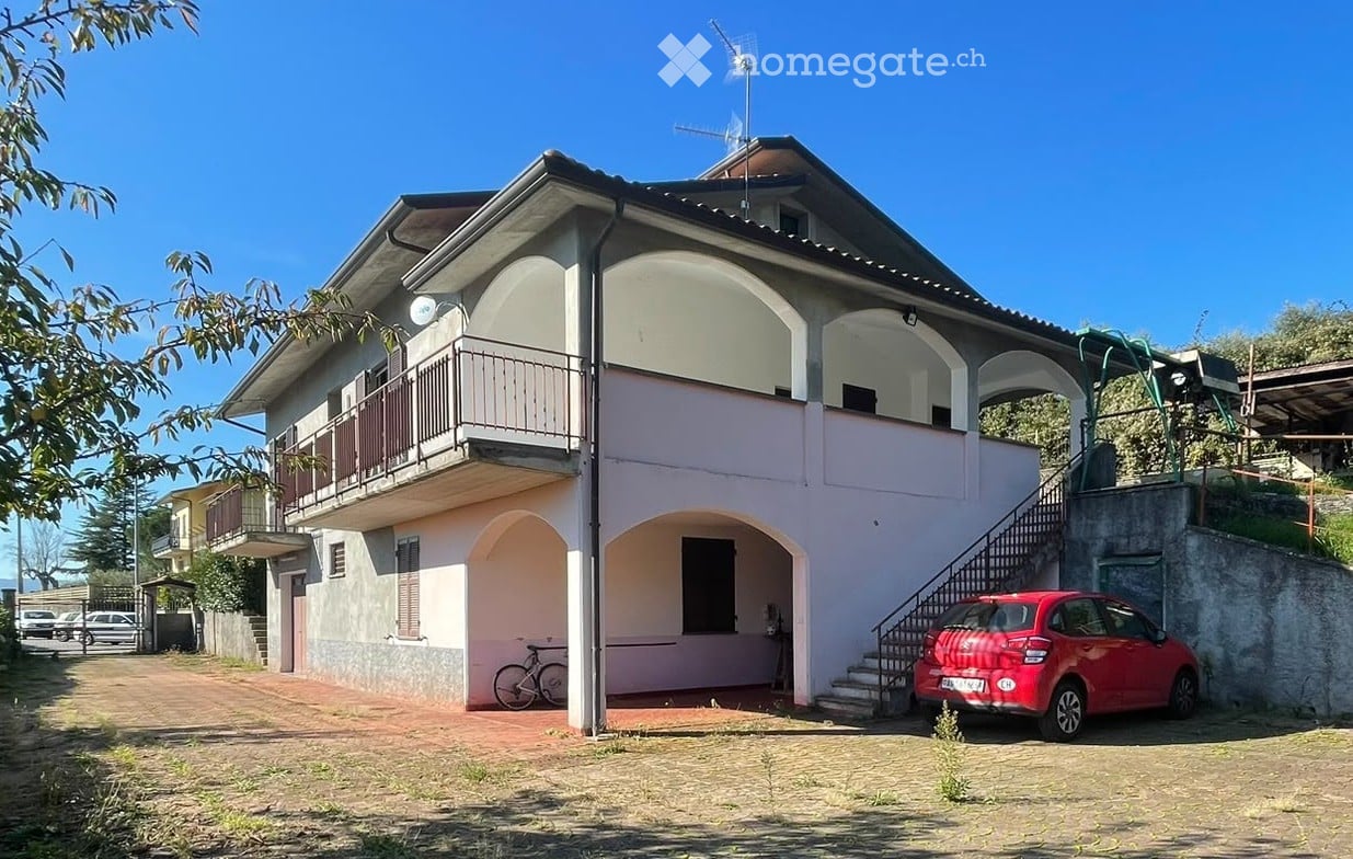 Two-story house with pink and white exterior, arched windows, balcony, and a red car parked in the driveway.