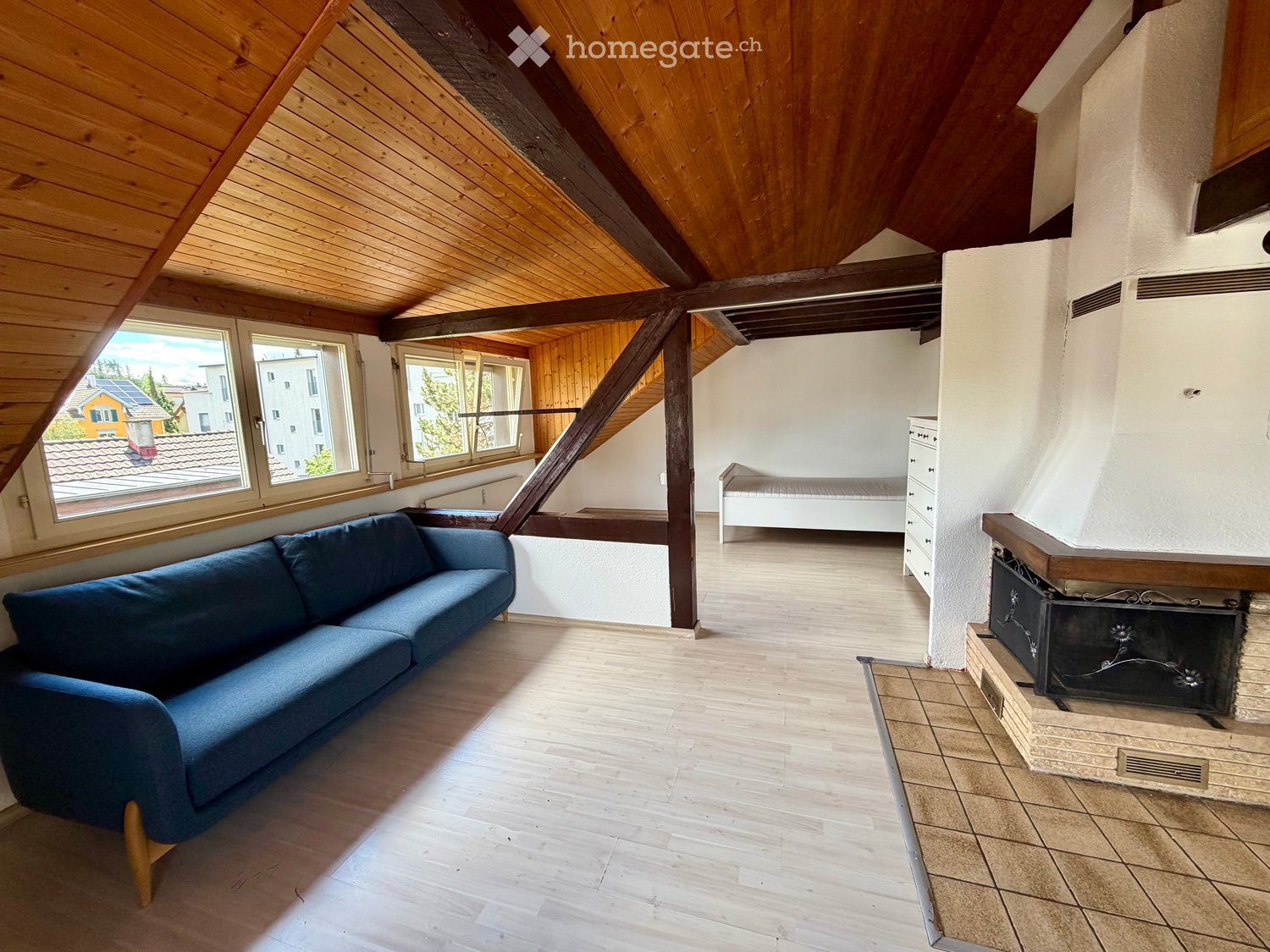 Living room with wooden ceiling beams, exposed wooden beams, large windows, fireplace, and a blue sofa.