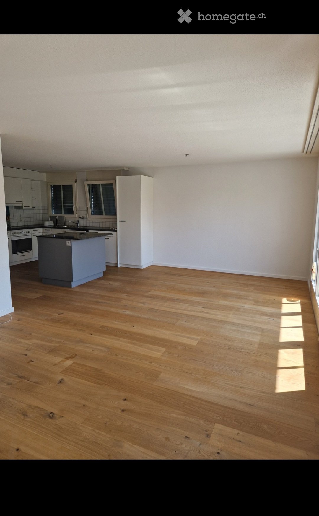 Empty kitchen with wooden flooring, white cabinets, and a central island. No furniture or appliances are present.