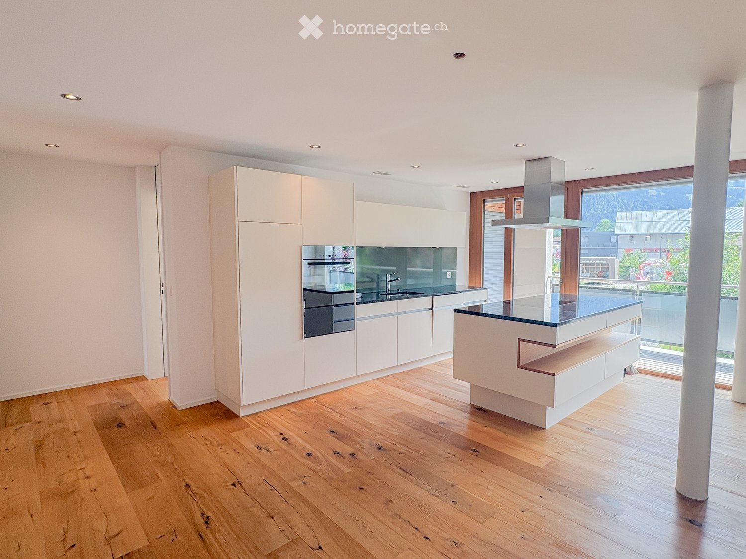 Modern kitchen with light-colored cabinets, a central island, and a sleek glass countertop. Features include a built-in oven, a range hood, and a sink with a modern faucet.