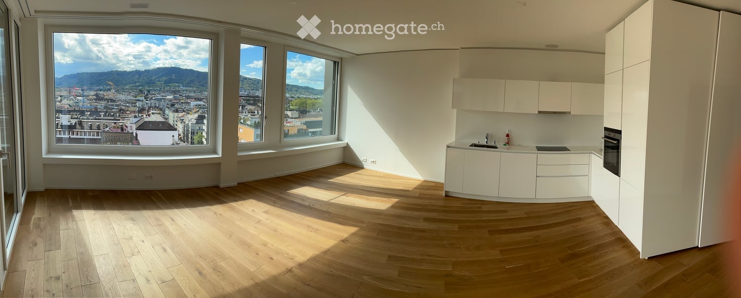 Modern kitchen with white cabinets, wooden flooring, and large windows offering a scenic city view.