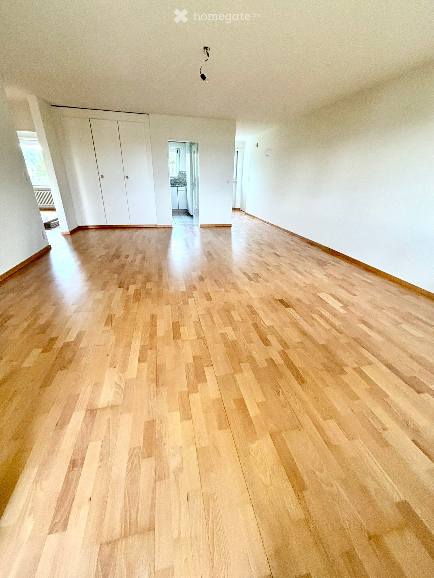 Empty room with light wooden flooring, white walls, and a white closet. The room is well-lit with natural light coming from a window on the left side.