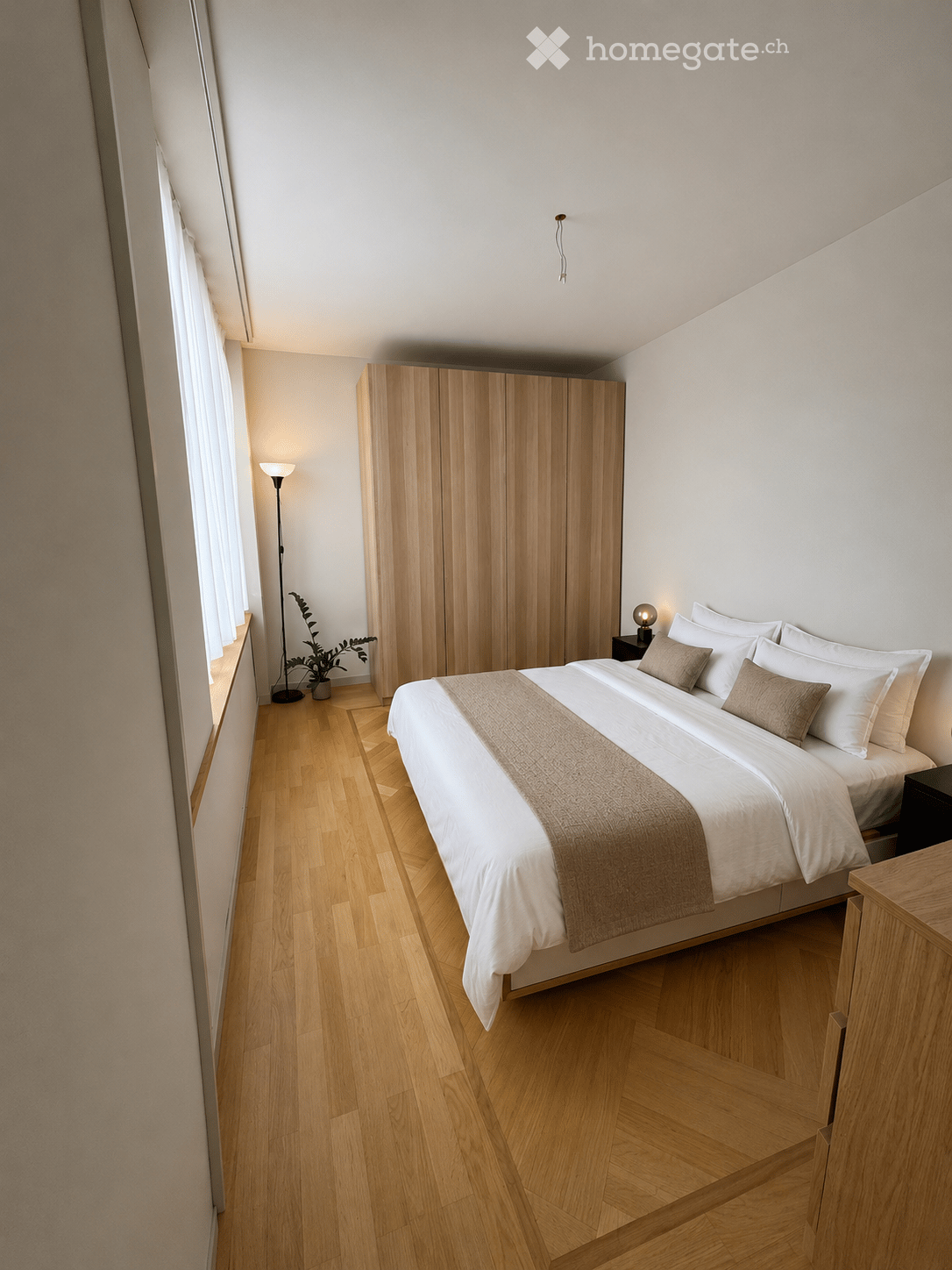 Modern bedroom with a large bed, white bedding, wooden wardrobe, nightstand, floor lamp, and a small plant near the window.