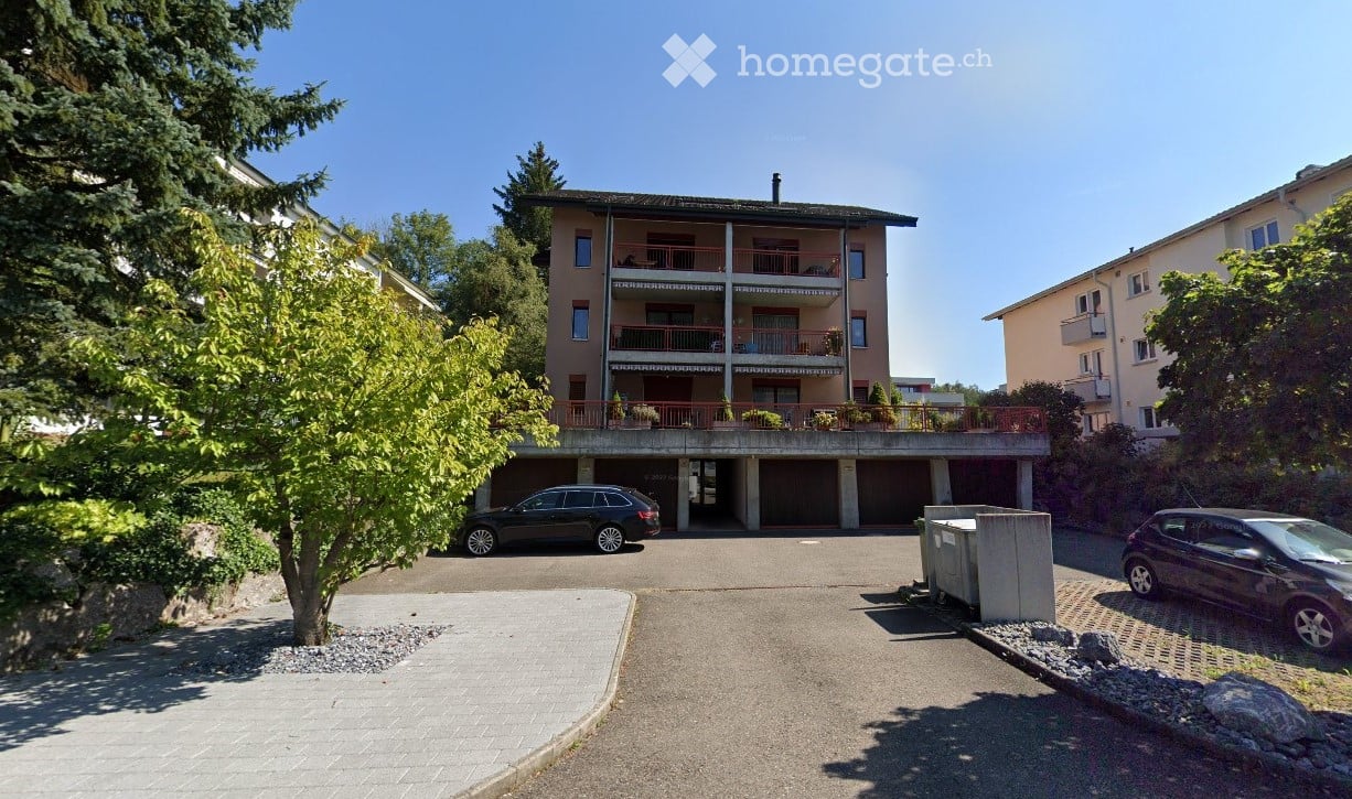 Multi-story apartment building with balconies, garage, and parking area.