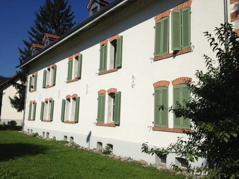 white building with green shutters, red brick trim, multiple windows, grassy lawn in front