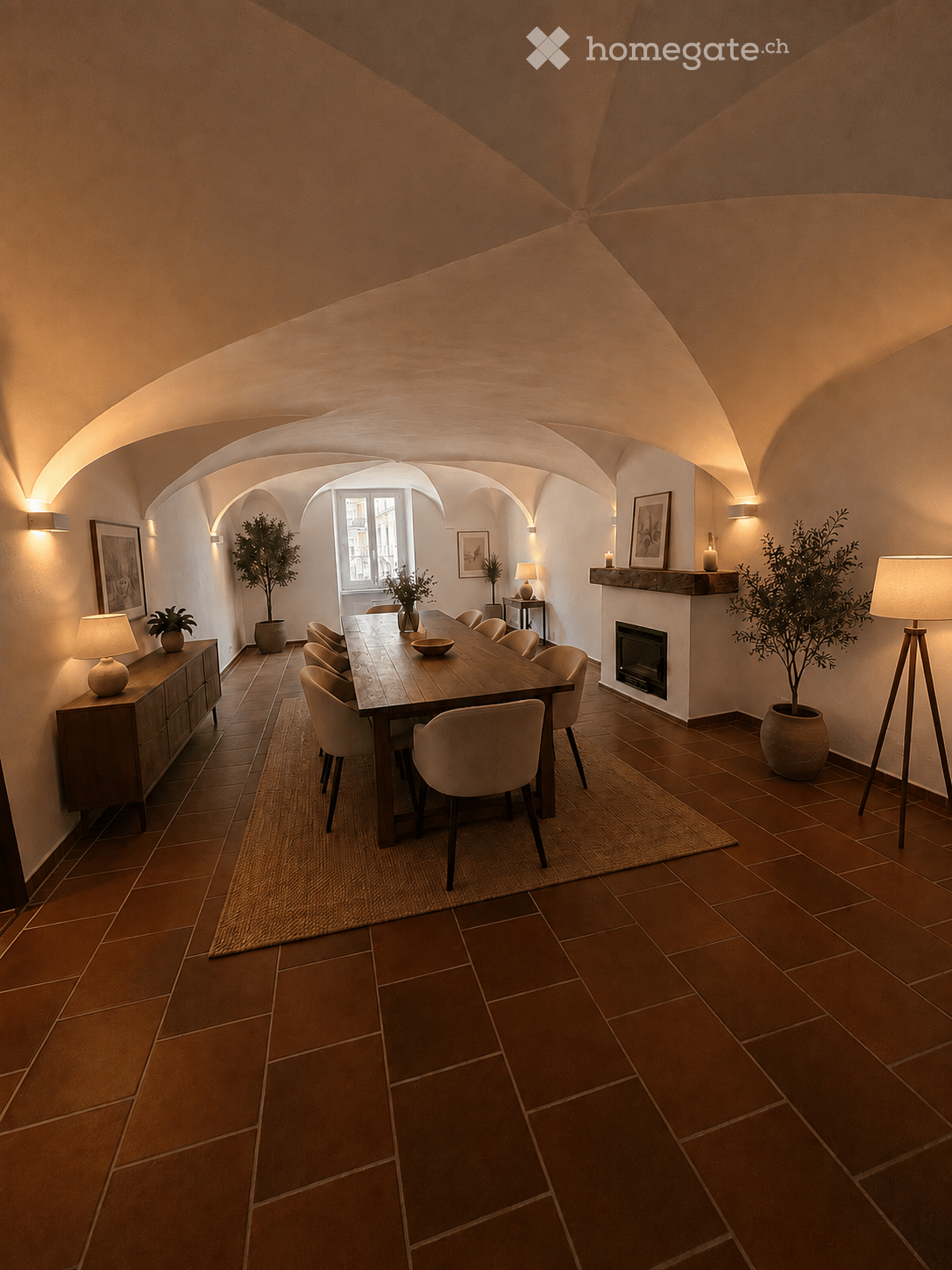 Elegant dining room with terracotta tiled floor, arched ceiling, fireplace, dining table with chairs, cabinet, lamps, and potted plants.