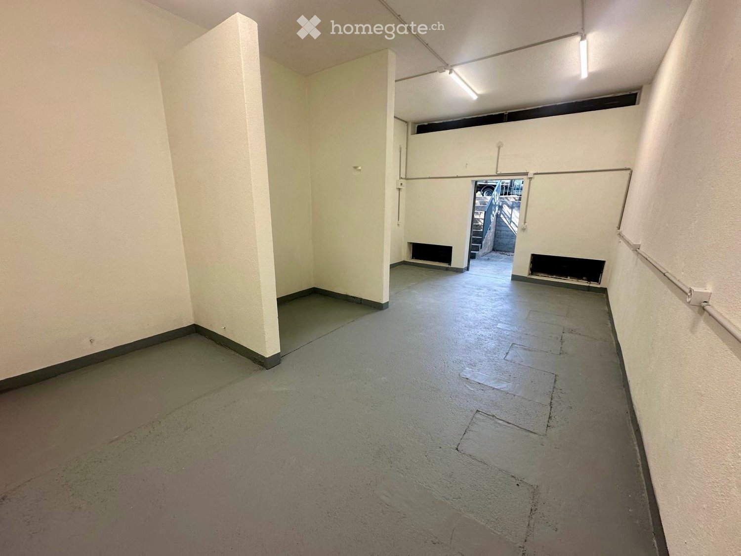Empty hallway with white walls, concrete floor, and a small opening leading to another area.
