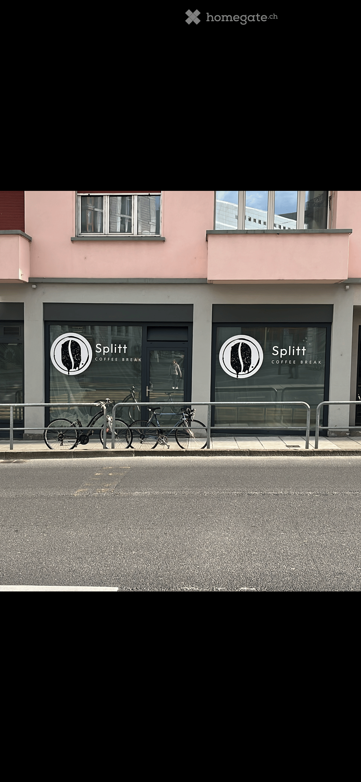 Pink building with two windows and two signages on front entrance, bicycles parked on metal railings in front.