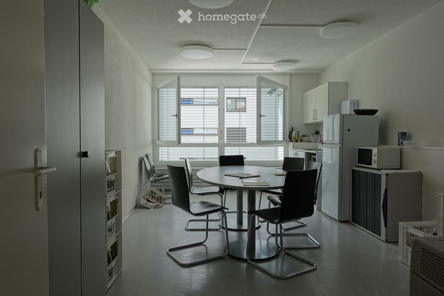 Modern, minimalist kitchen and dining area with a round table, six chairs, and modern appliances including a refrigerator and microwave.