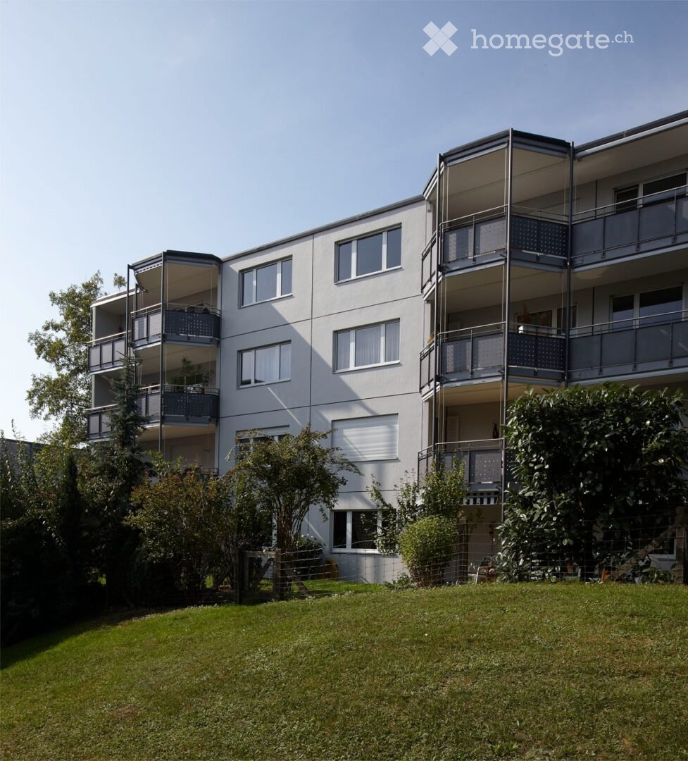 Modern multi-story apartment building with balconies, large windows, and surrounding greenery.