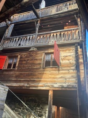 Traditional wooden chalet with exposed beams, wooden balconies, and red shutters.