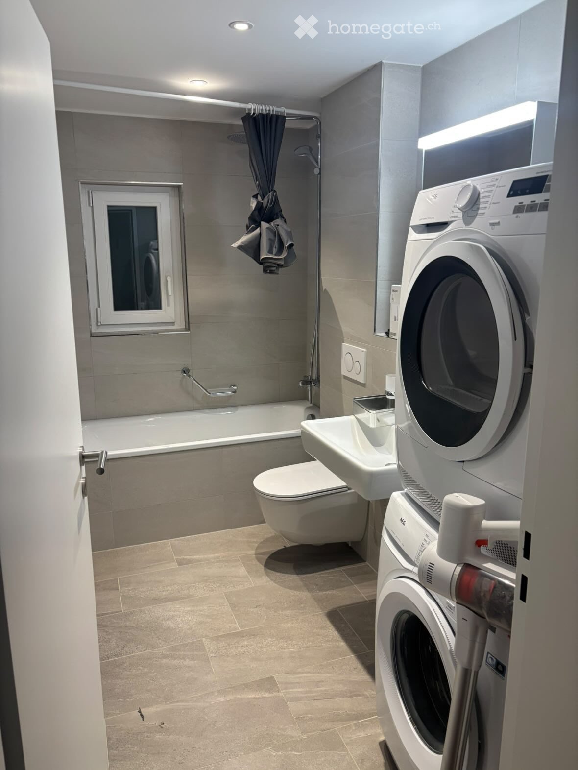 Modern bathroom with a bathtub, toilet, sink, washing machine, dryer, and a shower area with a curtain.