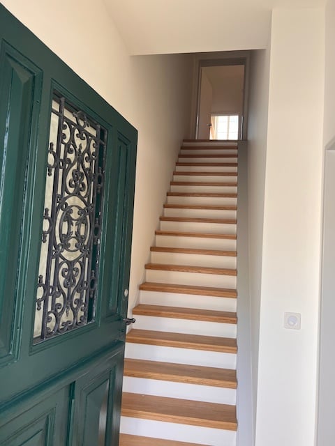 Wooden staircase with white walls and a green door with decorative wrought iron design.