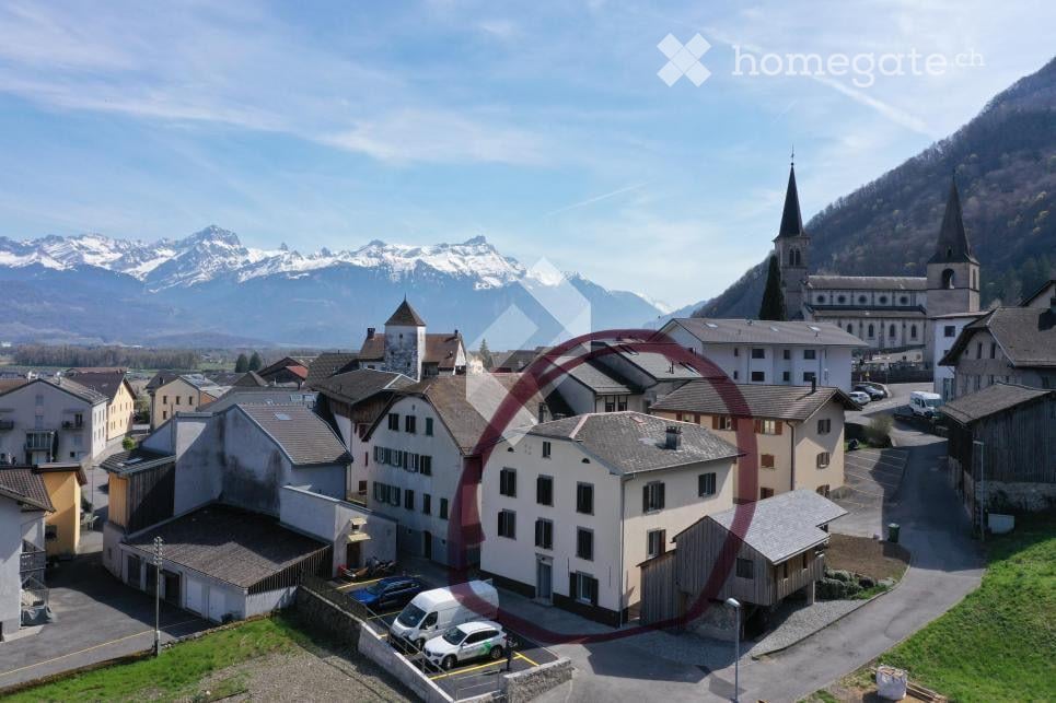 Aerial view of a small village with traditional houses, a church, and snow-capped mountains in the background.