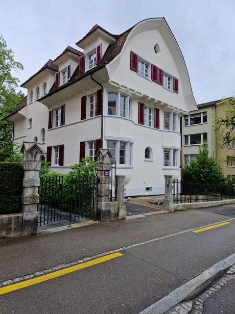3 story house, white exterior, red shutters, brown roof, black gate, stone pillars, garden, street