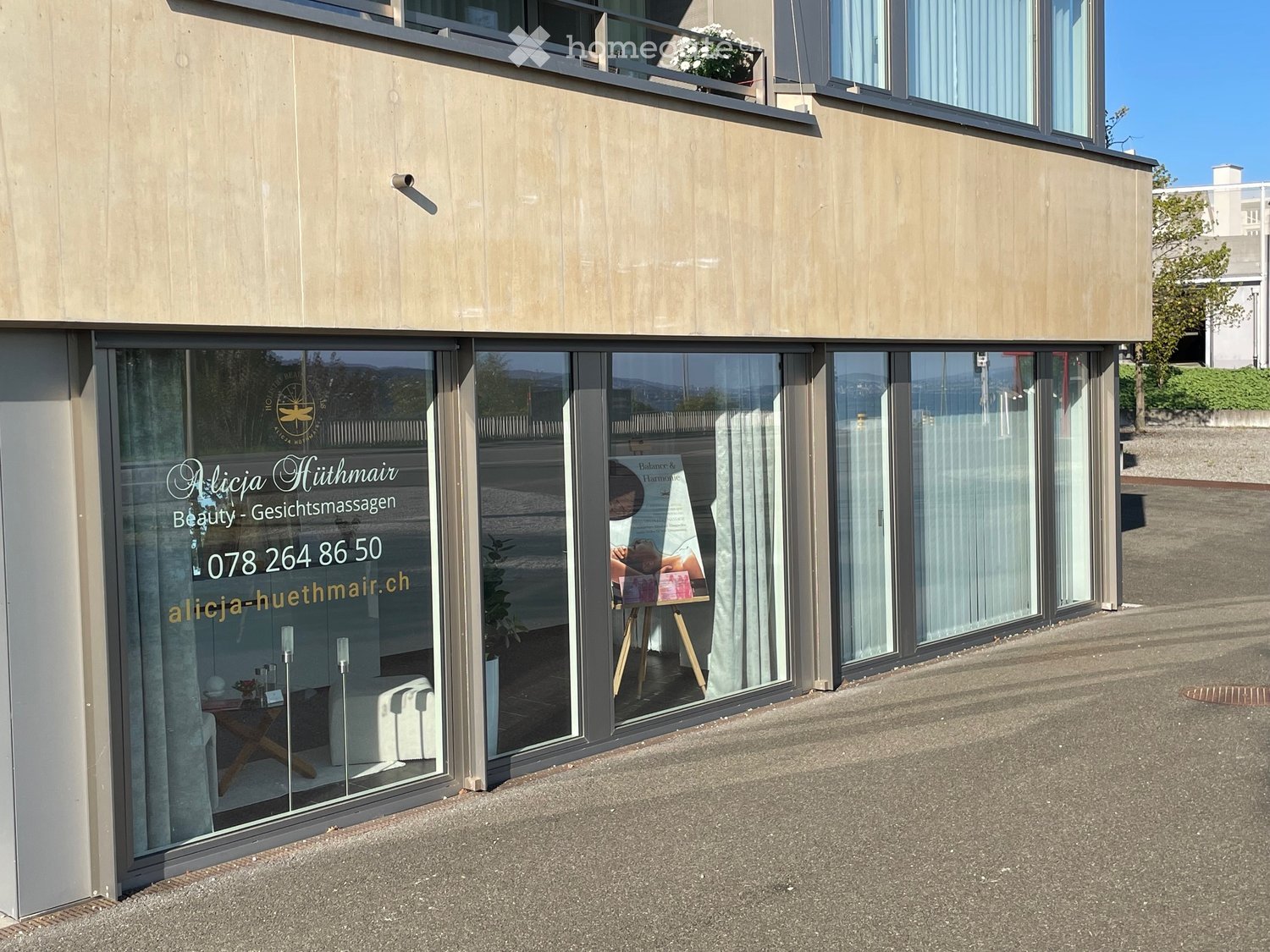 Modern building facade with large glass windows and a balcony, featuring a beauty salon interior visible through the glass.