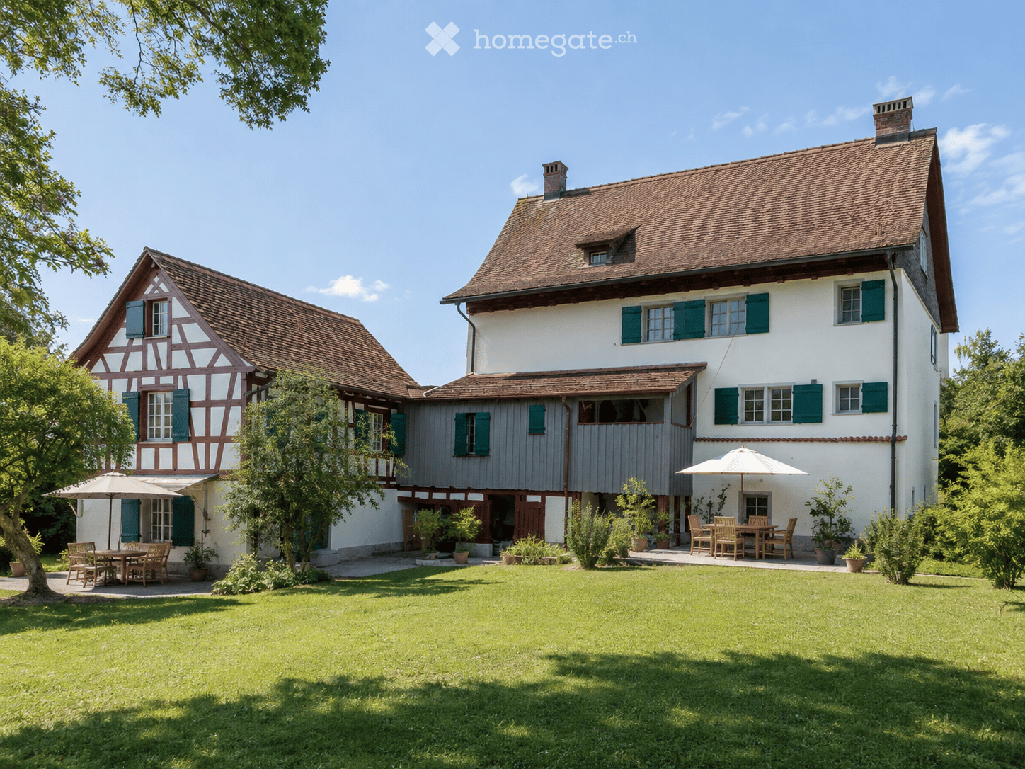 Two-story house with a traditional half-timbered design and a modern white facade, surrounded by a well-maintained lawn and outdoor seating areas.