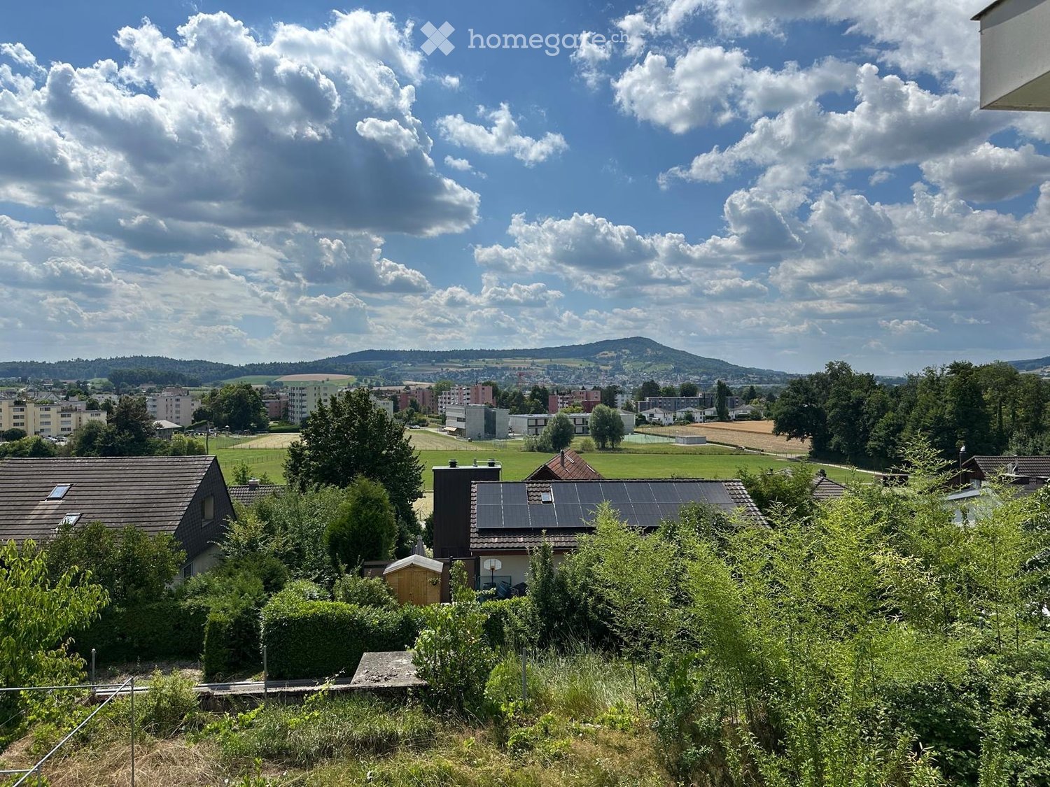 A panoramic view of a suburban neighborhood with houses, trees, and a distant landscape under a partly cloudy sky.
