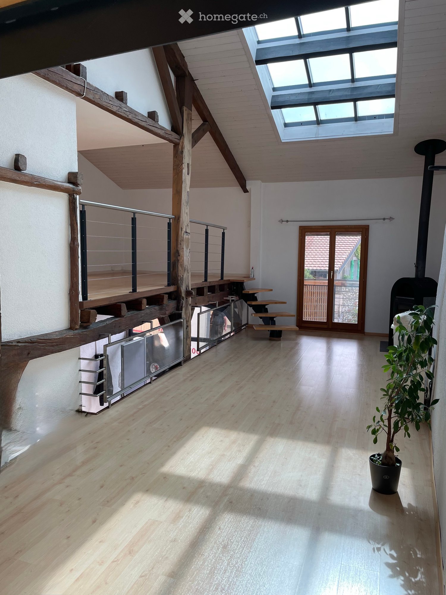 Bright, open hallway with wooden flooring, white walls, and a skylight. Features a staircase with wooden railings and a small table near the entrance.