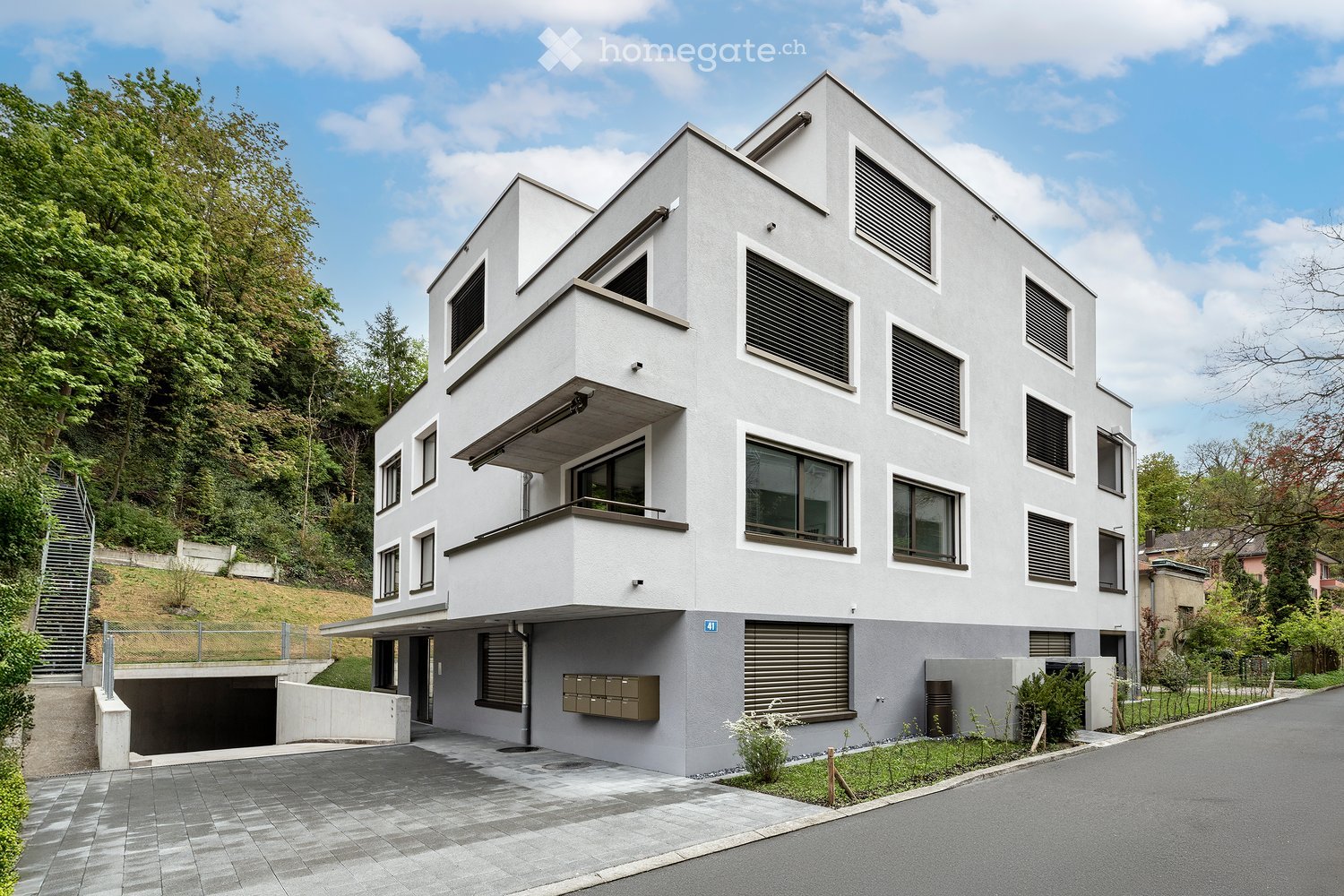 Modern two-story house with white facade, large windows, raised ground floor, and garage entrance.