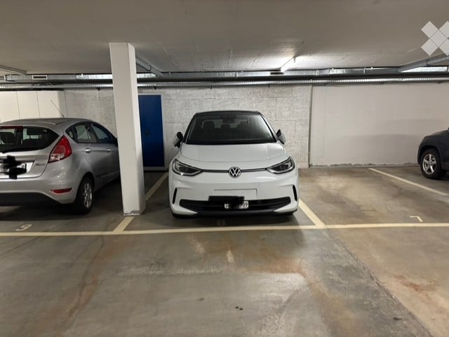 underground parking lot with three cars parked, white walls, yellow markings