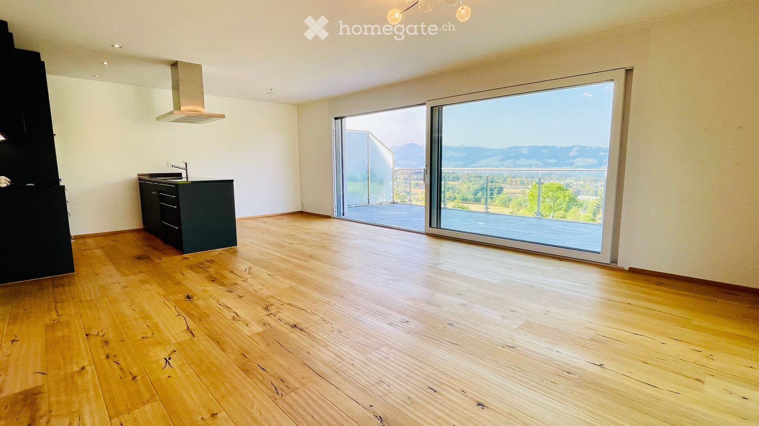 Empty room with wooden flooring, white walls, and a large sliding glass door leading to a balcony with a scenic mountain view.